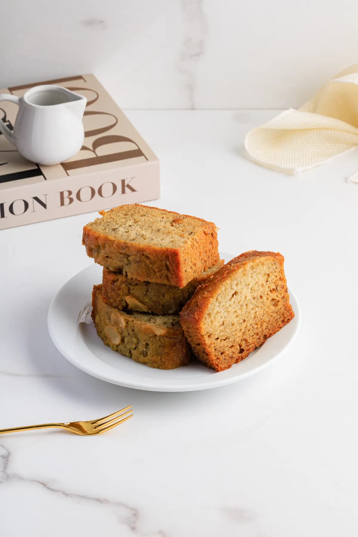 Slices of fresh banana bread on a white plate with a gold fork.