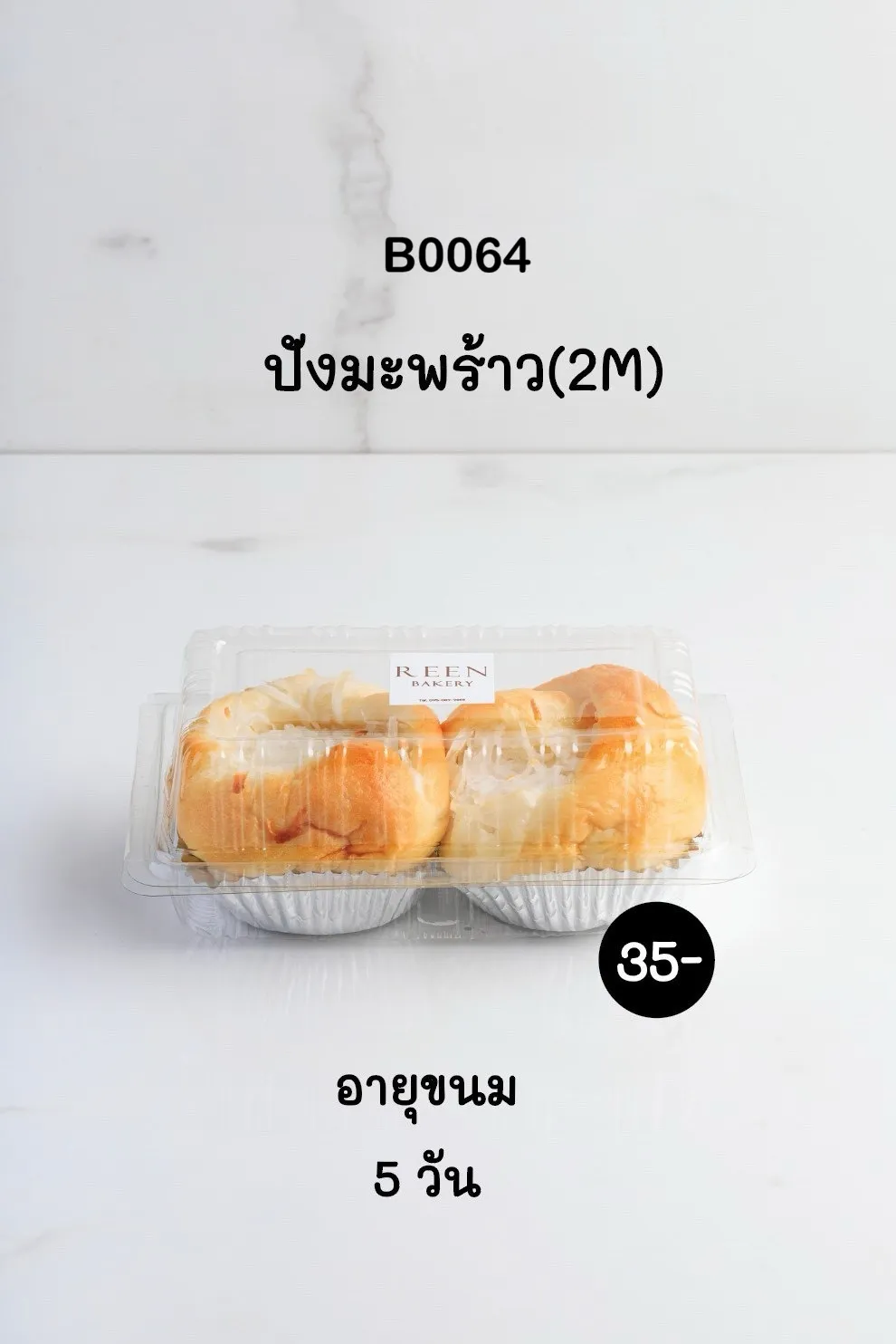 ขนมปังมะพร้าว 2 ชิ้น วางอยู่ในกล่องพลาสติกใส มีโลโก้ REEN BAKERY ด้านบน ขนมปังสีทองอมน้ำตาลโรยมะพร้าวขูดสีขาวบนพื้นหลังสีขาว