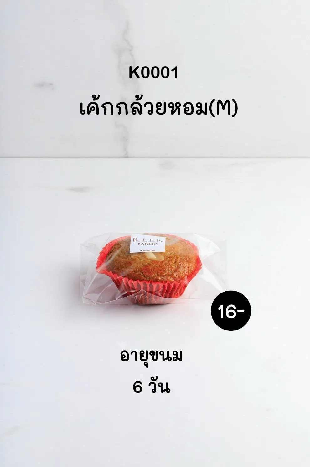 เค้กกล้วยหอมขนาดกลางในถ้วยกระดาษสีแดง ห่อด้วยพลาสติกใสพร้อมฉลาก REEN BAKERY วางอยู่บนพื้นผิวสีขาว